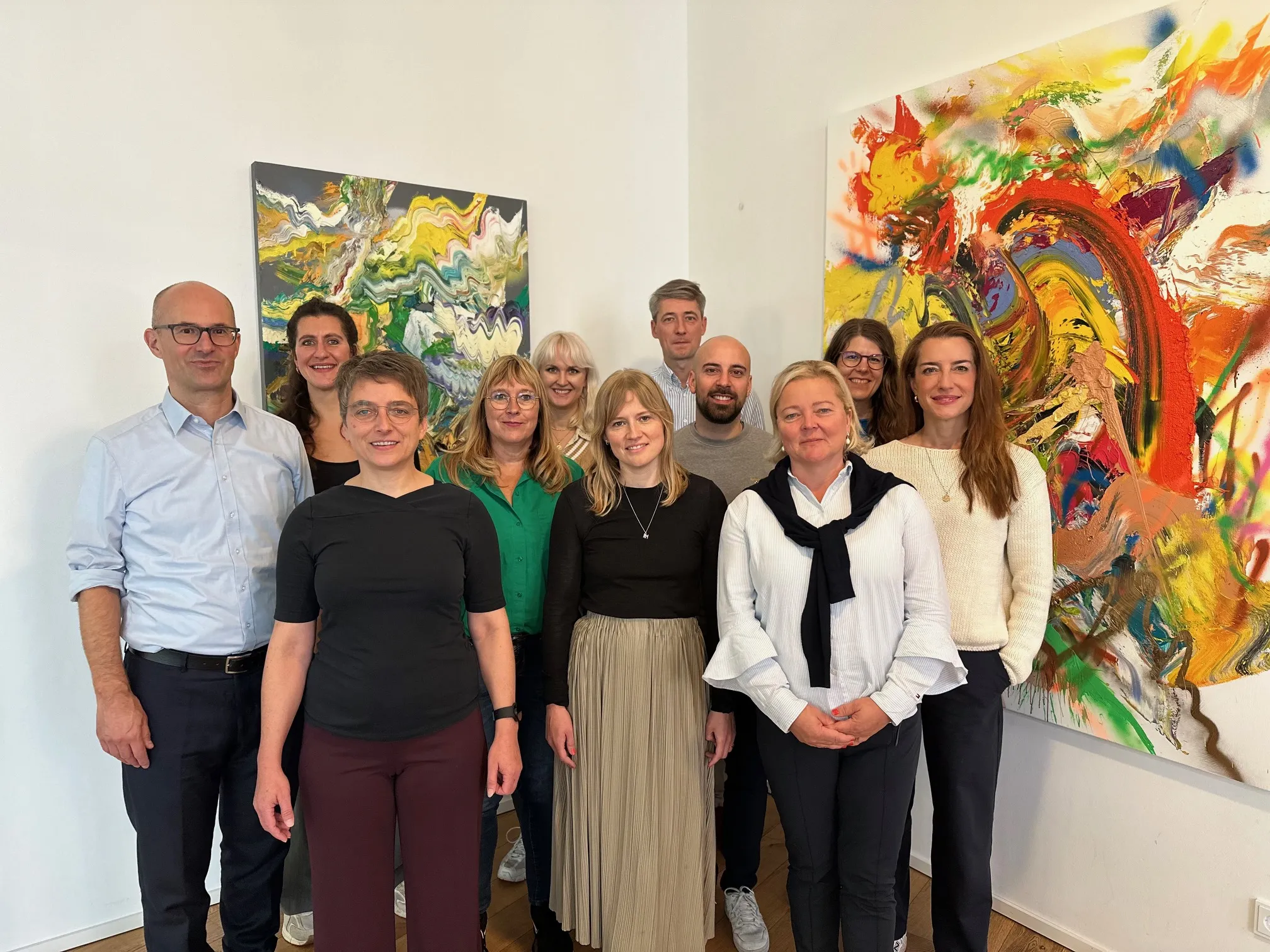 Gruppenfoto des GEN NOW Teams vor zwei abstrakten Kunstwerken an einer weißen Wand